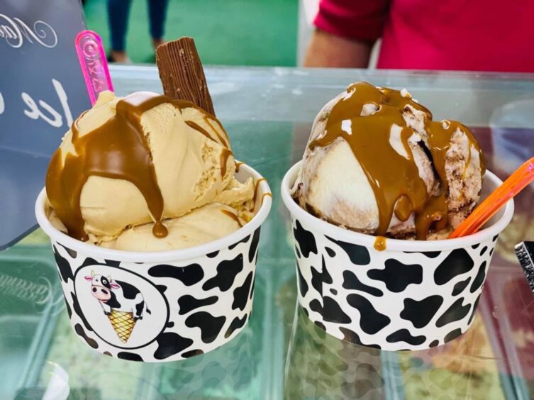 Two tubs of ice cream sit on the counter at Scoops of Moo, a must stop off on your tour of the Montrose food and drink scene. The tubs have a cow-themed pattern and a caramel sauce is dribbled over the ice cream. 