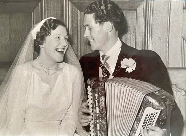 Joan and Jimmy Blue, she is wearing wedding dress, he is holding an accordion