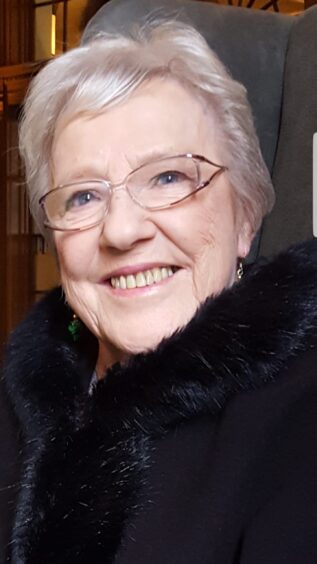 Joan Blue in later life, smiling in a dark coat