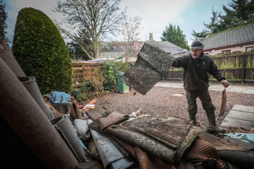 David Scott throws ruined carpets and flooring into a pile outside his flooded home. 