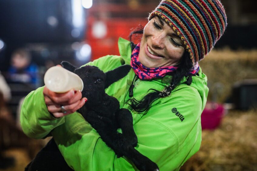 Gayle bottle feeds a tiny black lamb. Image: Mhairi Edwards.