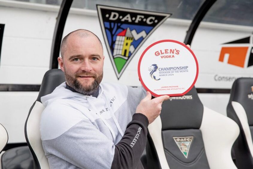 Dunfermline Athletic F.C. manager James McPake sits in the East End Park dugout and holds up his manager of the month award.