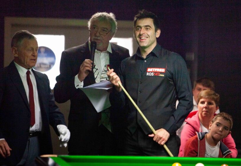 John Virgo and Ronnie O'Sullivan beside a snooker table at Shotz in 2016, with the referee and audience in the background