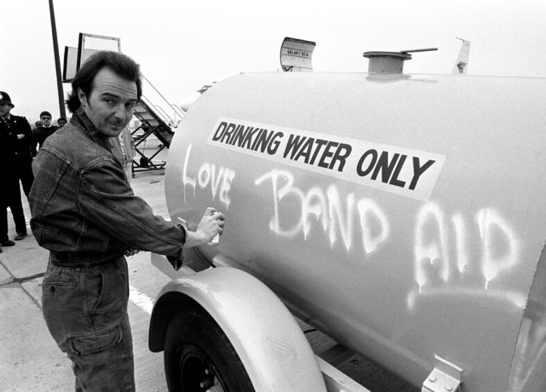 Midge Ure, 31 of the Rock Group Ultravox, who with Bob Geldof wrote the Band Aid single 'Do They Know It's Christmas?', spraying a message on a water tanker at Gatwick Airport.