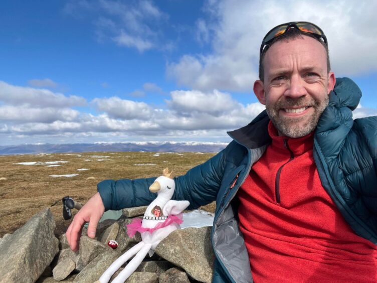 Allan MacRaild and soft toy swan next to Cairn on mountaintop