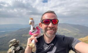 Allan MacRaild posing on Scottish mountain top with white swan soft toy