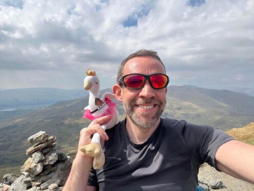 Allan MacRaild posing on Scottish mountain top with white swan soft toy