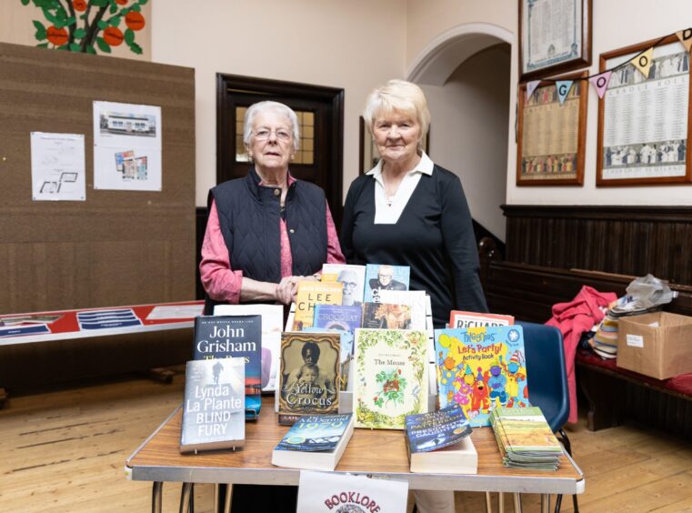 Two women standing behind table covered in books
