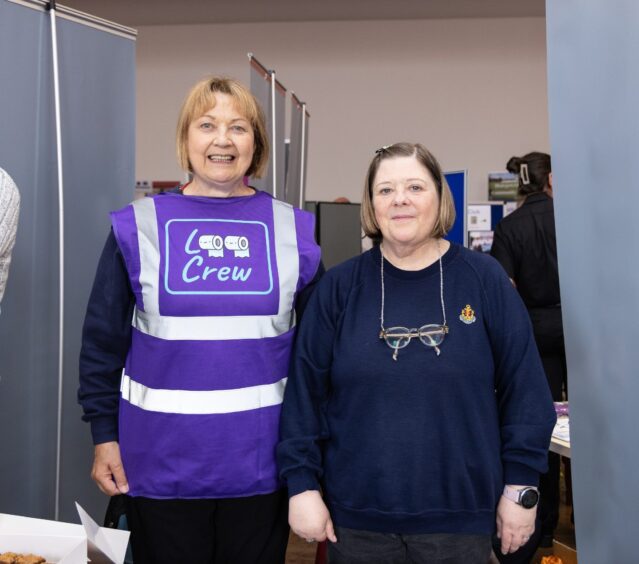 Two woman, one wearing a tabard with the 'loo crew' logo