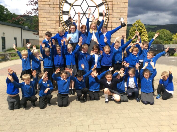 Young children in blue school uniforms raising arms for the camera at Aberfeldy Mod in 2019
