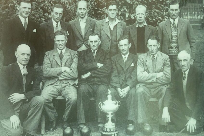 Black and white photo of Abernethy bowling club members standing and seated behind a trophy in 1947