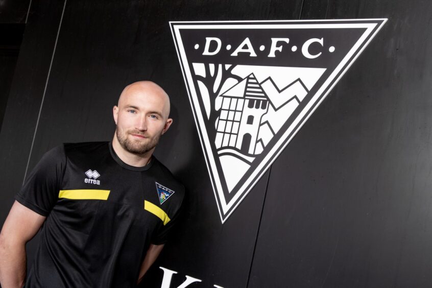 Chris Kane stands in front of a large Dunfermline Athletic FC badge.