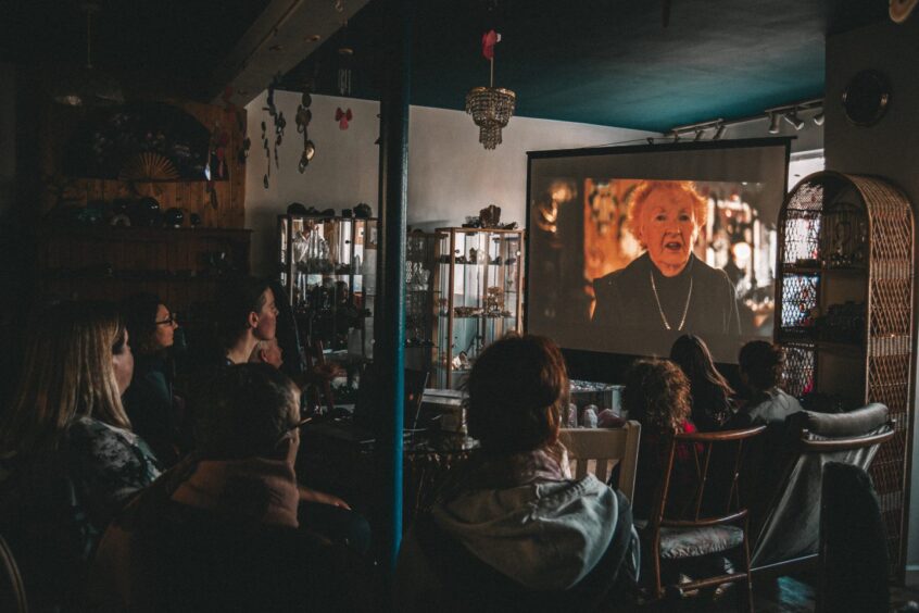 People in darkened Amethyst Cathedral shop, watching Elisabeth Michael on projector screen