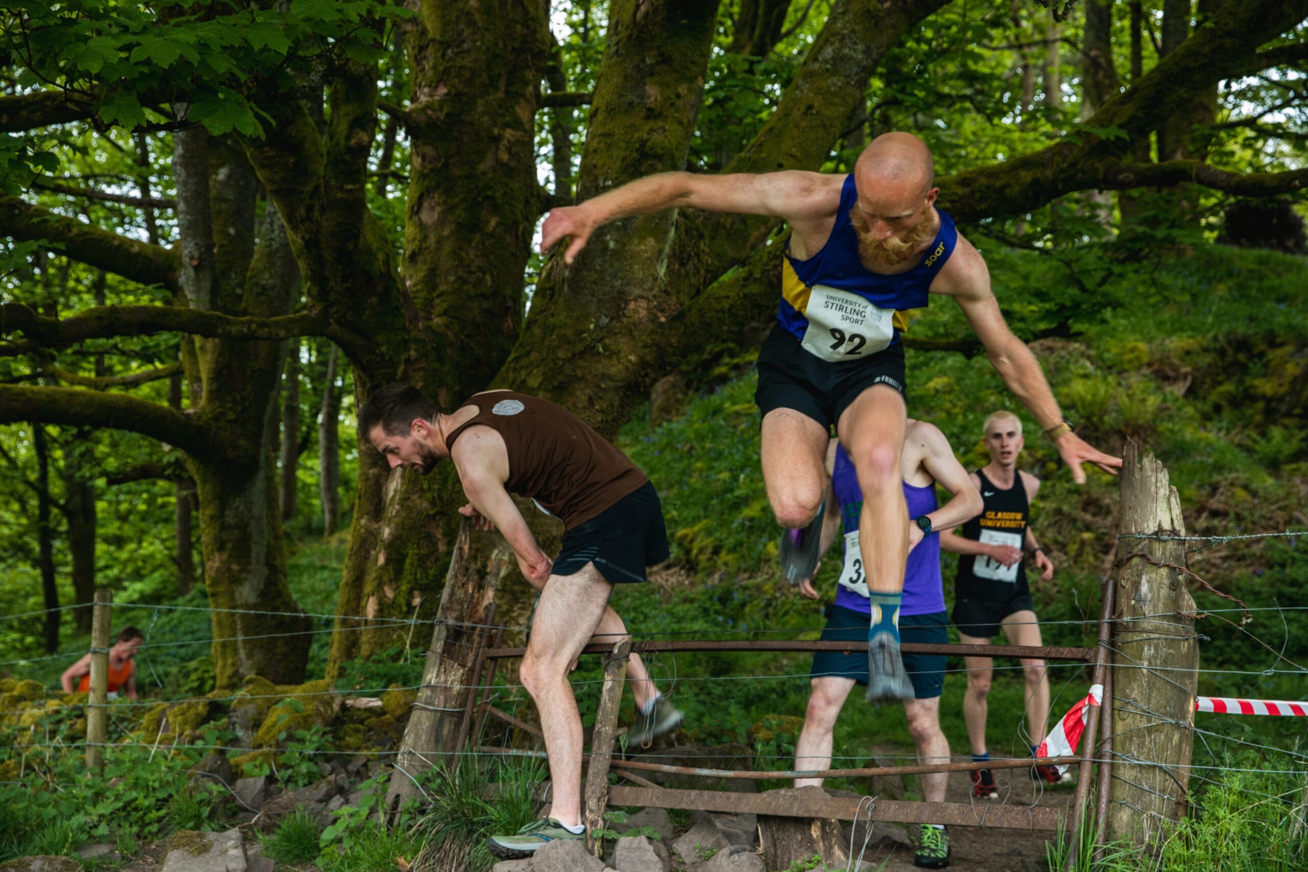 Runners jump over a style as they come out of the woods