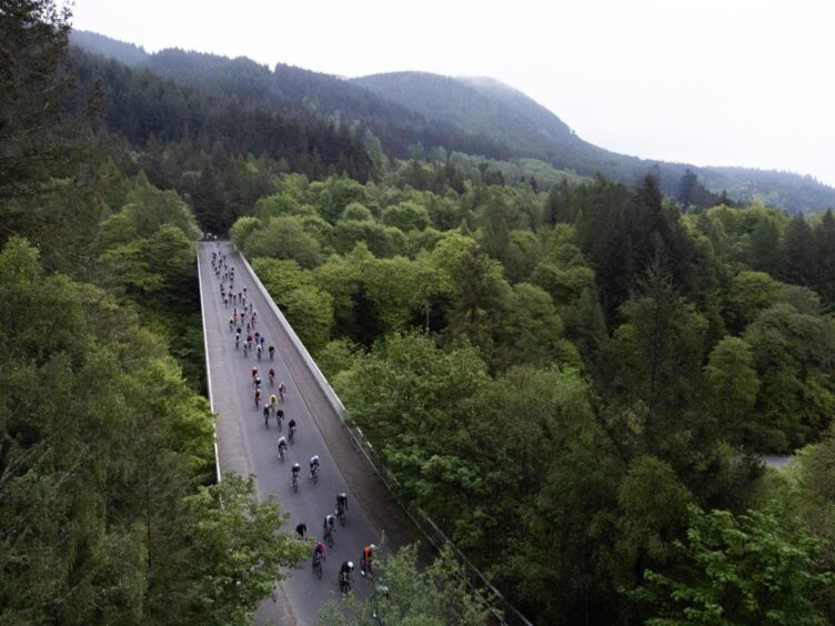 Aerial photo showing cyclists riding over bridge surrounded by mountains and forests