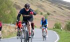 Cyclist giving thumbs-up to camera while rising through mountainous Perthshire scenery
