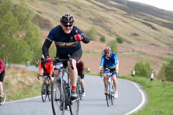 Cyclist giving thumbs-up to camera while rising through mountainous Perthshire scenery