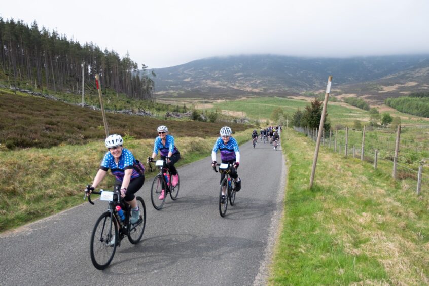 Cyclists riding through moorland and forests with misty mountains behind