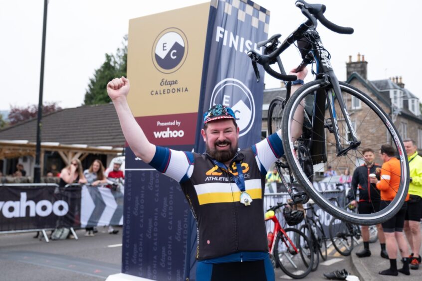 Smiling cyclist holding bike in one hand while giving victory salute
