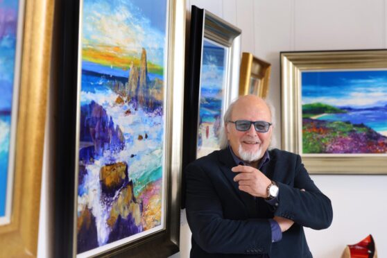 The artist Jolomo in front of a colourful seascape in Strathearn Gallery, Crieff
