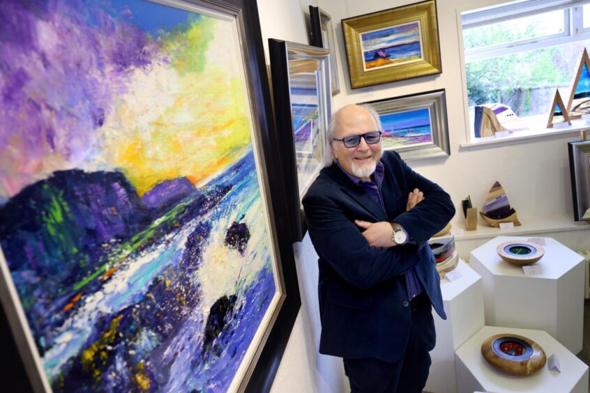 The artist Jolomo in front of a colourful seascape in Strathearn Gallery, Crieff