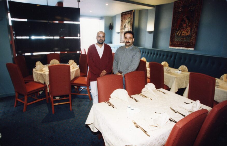 Two staff members standing behind a table and chairs in April 1996. 