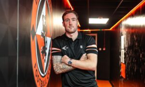 Kevin Holt leans against a wall featuring a large Dundee United crest