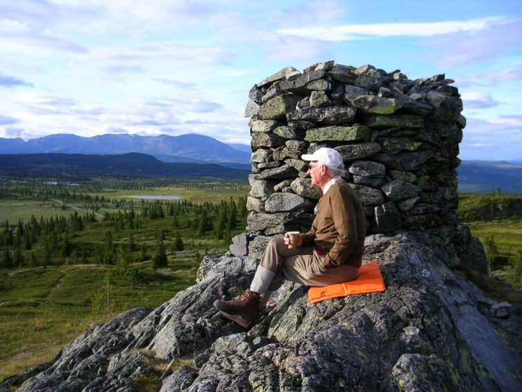John Walker seated next to Cairn on mountaintop