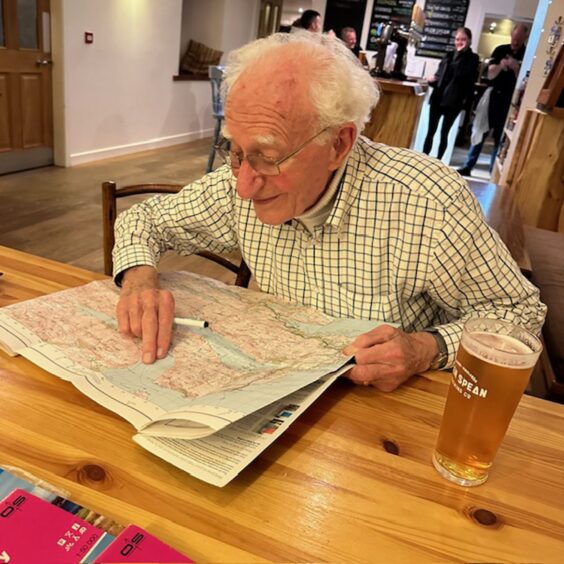 John Walker as an older man looking at map with pint glass by his side