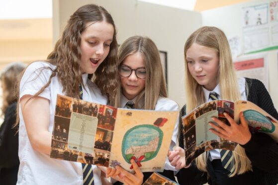 Three girls looking excitedly through comic book at Black Watch Museum