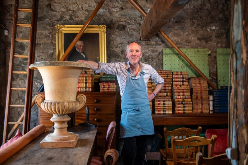 Tim Hardie in blue apron standing next to large urn in front of table covered in old books