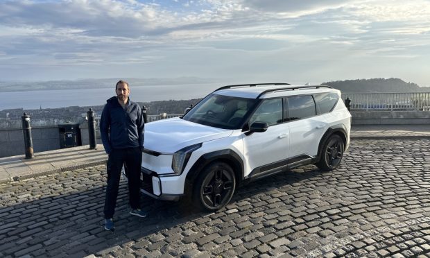 Jack McKeown beside a white Kia EV9 at the top of a Dundee hill