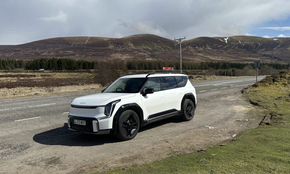 The Kia EV9 sits by the side of the road at Dalwhinnie, with hills in the background