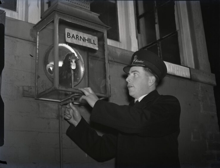 A staff member lighting a lamp inside a glass cabinet at Barnhill Railway Station before the final journey.