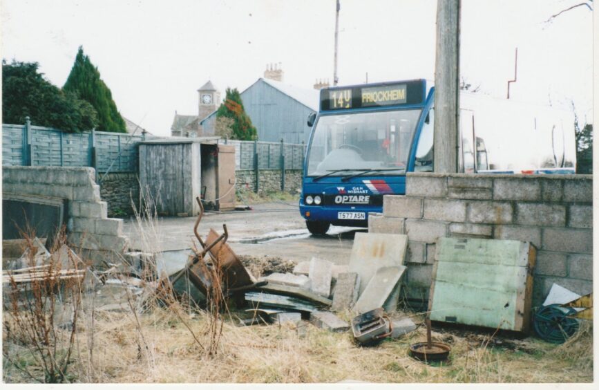 A single decker bus beside a damaged wall in the yard