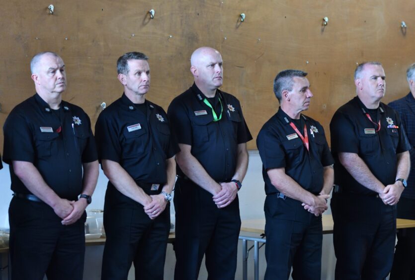 Firefighters lined up in uniform listening to speeches at ceremony