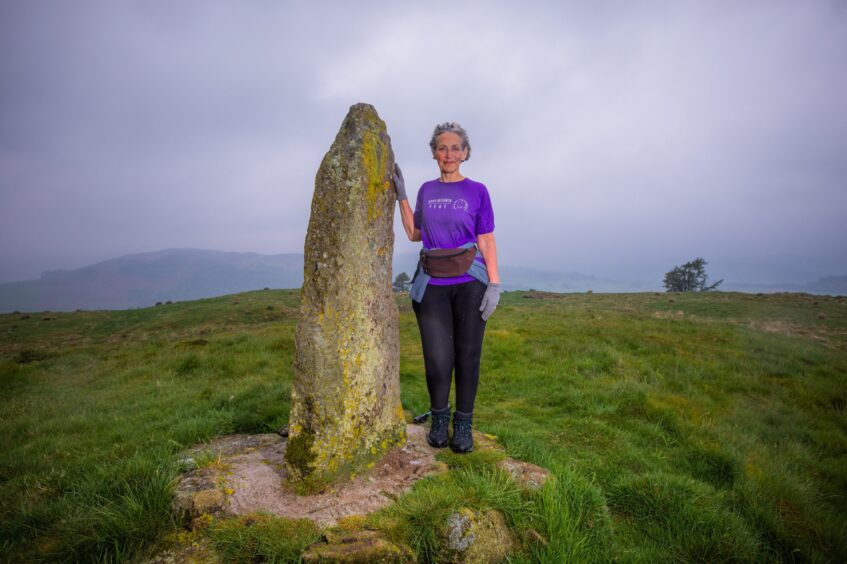 Dee Thomas standing next to tall standing stone on top of hill