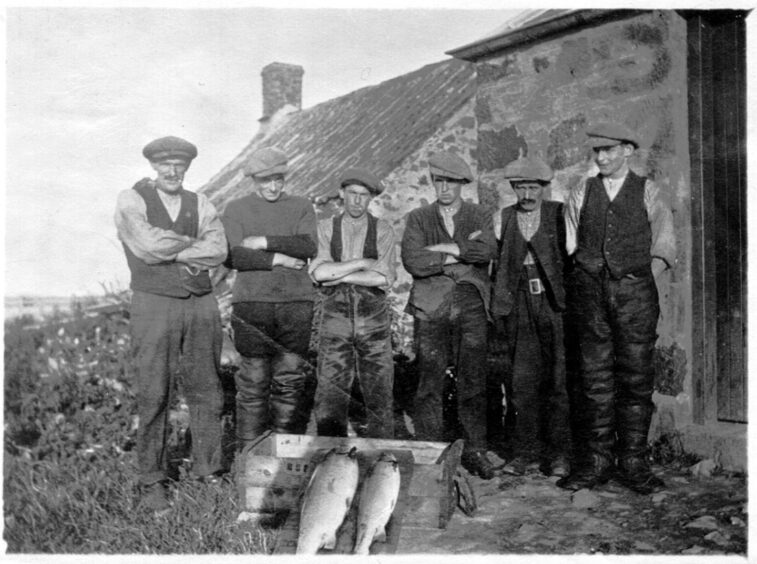 Group of men standing outside salmon bothy with two large fish at their feet