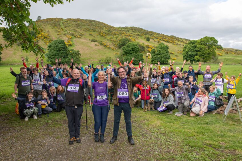 Dee Thomas, Colin Graham and Craig Stobo, standing in front of group of cheering friends with hill behind