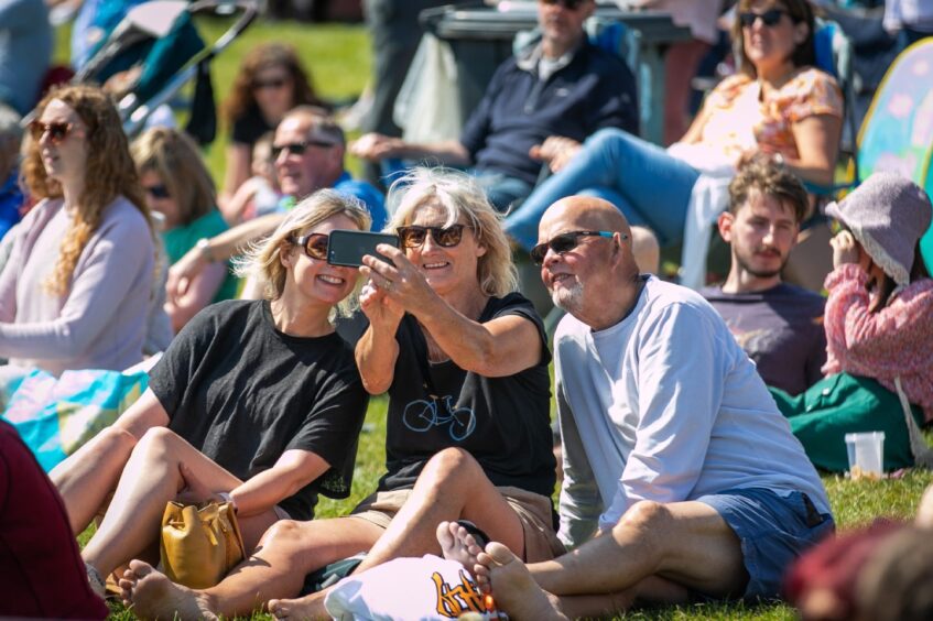 Three people smile for a selfie as they sit in the sun at Dundee festival Westfest in 2023.
