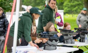 Children shooting air rifles watched by adults