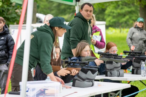 Children shooting air rifles watched by adults