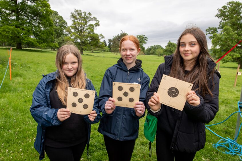 Three girls holding paper targets with shots in them