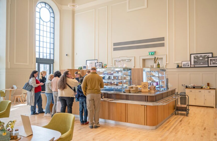 Stone cafe counter with customers queuing for coffees and cakes