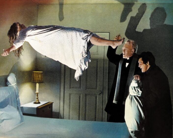 A possessed girl levitates above her bed as two priests perform an exorcism in a scene from The Exorcist, 1973.