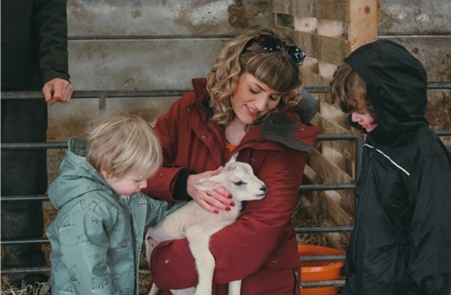 Woman showing a lamb to two children.