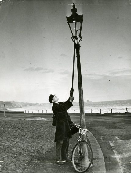 A lamplighter reaches up to light a lamp on Harbour Board 