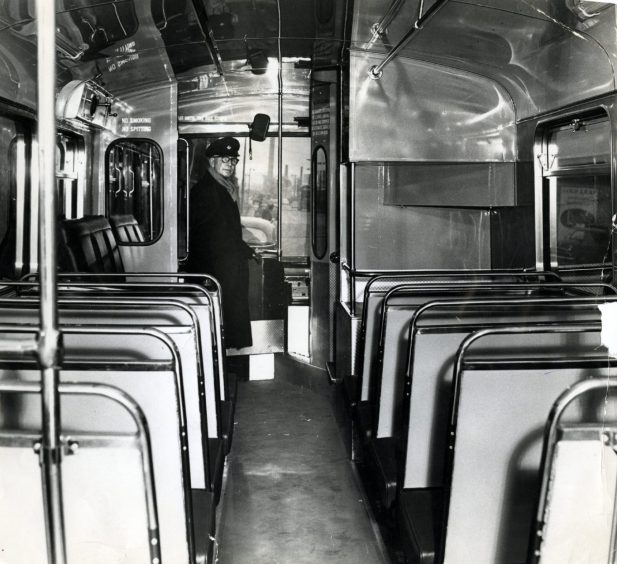 a conductor stands at the front of an empty Dundee Corporation bus 