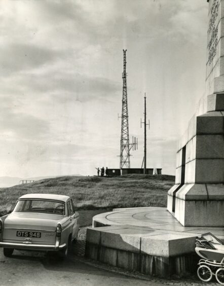 A car parked beside the memorial at the top of Dundee Law, with a TV mast in the distance