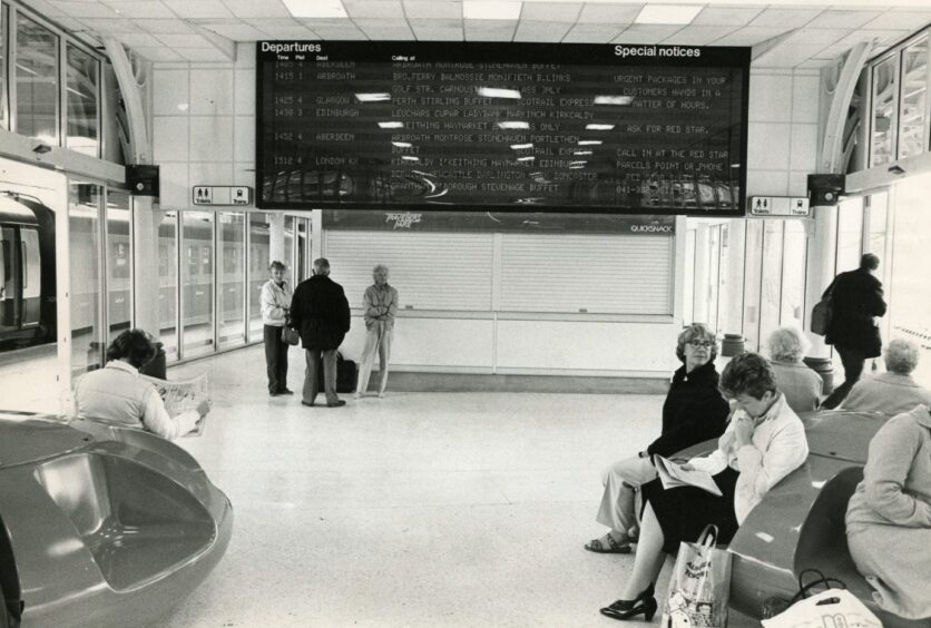people sit and stand in the station's waiting area with the departures board in 1985.